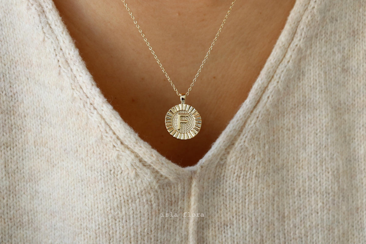 gold fluted medallion circular pendant featuring a stylized letter 'F' 